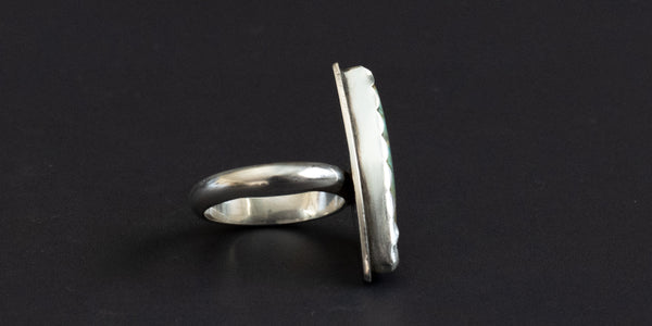 Side view of a turquoise ring with silver band and serrated bezel on a black background