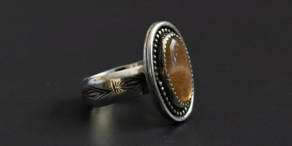 Side view of an oval sunstone set in handmade ring of .925 sterling silver with a hand stamped ring band