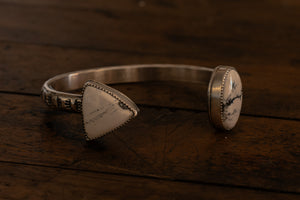 A triangle and an oval black and white stone set on either end of a cuff bracelet to appear floating