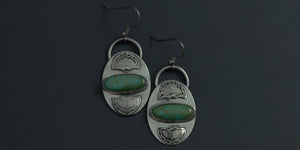 Oval, horizontal kingman turquoise stones set in a pair of handmade sterling silver earrings with hand stamped fan detailing above and below the stone 