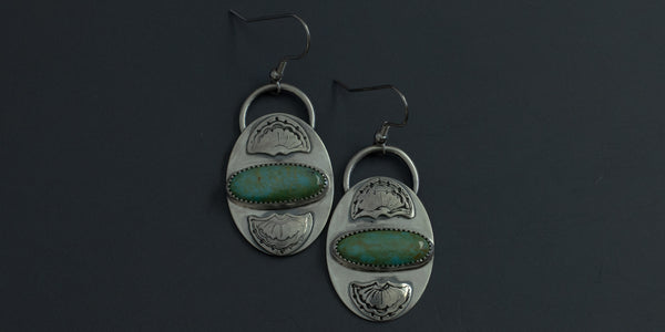 Oval, horizontal kingman turquoise stones set in a pair of handmade sterling silver earrings with hand stamped fan detailing above and below the stone 
