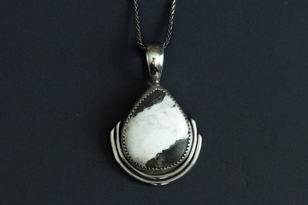 Teardrop shaped white buffalo stone set in .925 sterling silver on a black background