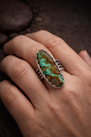 #8 Turquoise oval stone set in .925 sterling silver with a scalloped bezel and wide ring band shown on the middle finger of a hand