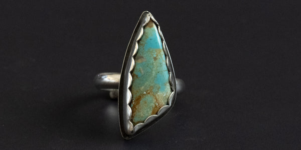 Turquoise ring with silver band and serrated bezel on a black background