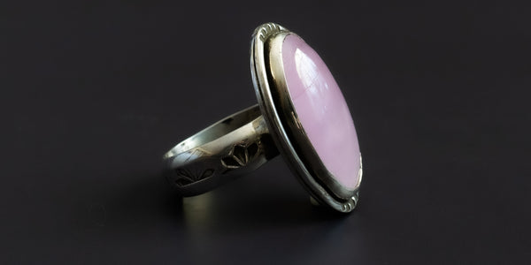Side view of a handmade sterling silver ring with an oval shaped, pink, kunzite stone set in a plain bezel and a hand-stamped ring shank