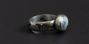 side view of an oval moss agate stone set in a handmade sterling silver ring with a plain bezel and hand stamped ring shank
