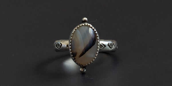 oval moss agate stone set in a handmade sterling silver ring with a serrated bezel and hand stamped ring shank