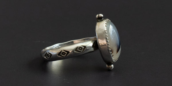 side view of an oval moss agate stone set in a handmade sterling silver ring with a serrated bezel and hand stamped ring shank