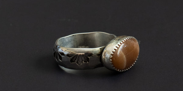 Side view of an oval sunstone set in a sterling silver handmade ring with a hand stamped ring band