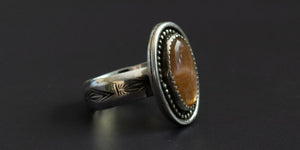 Side view of an oval sunstone set in handmade ring of .925 sterling silver with a hand stamped ring band